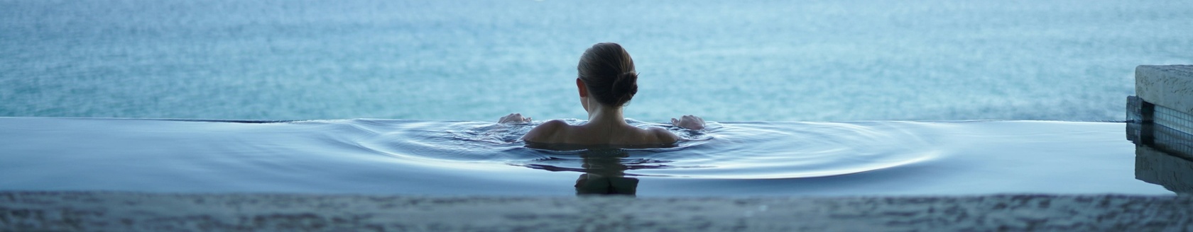 Person in infinity pool, looking at ocean.