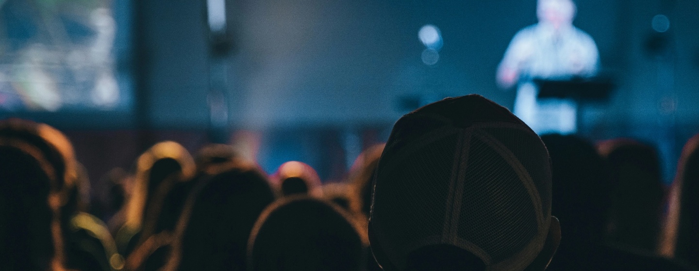 Attendees pay attention to a speaker on the main stage of a conference.