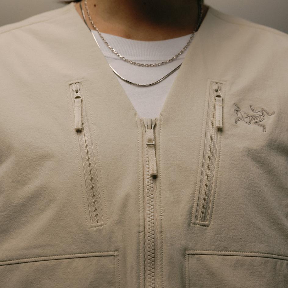 Beige Arc'teryx vest over a white t-shirt with two silver necklaces.