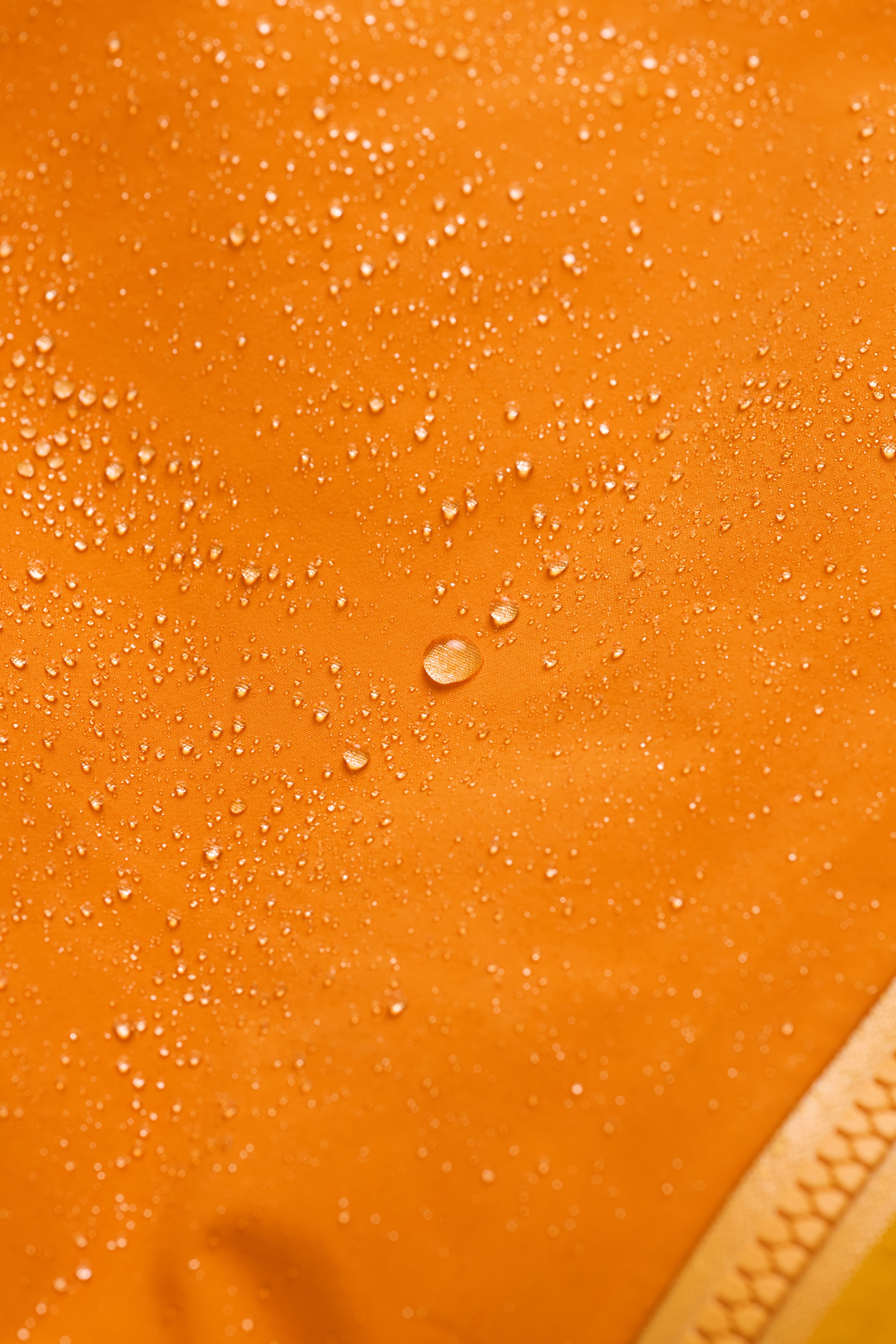 Water droplets beading on a bright orange waterproof fabric.