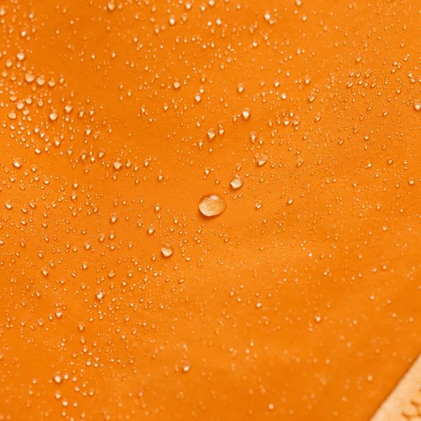 Water droplets beading on a bright orange waterproof fabric.
