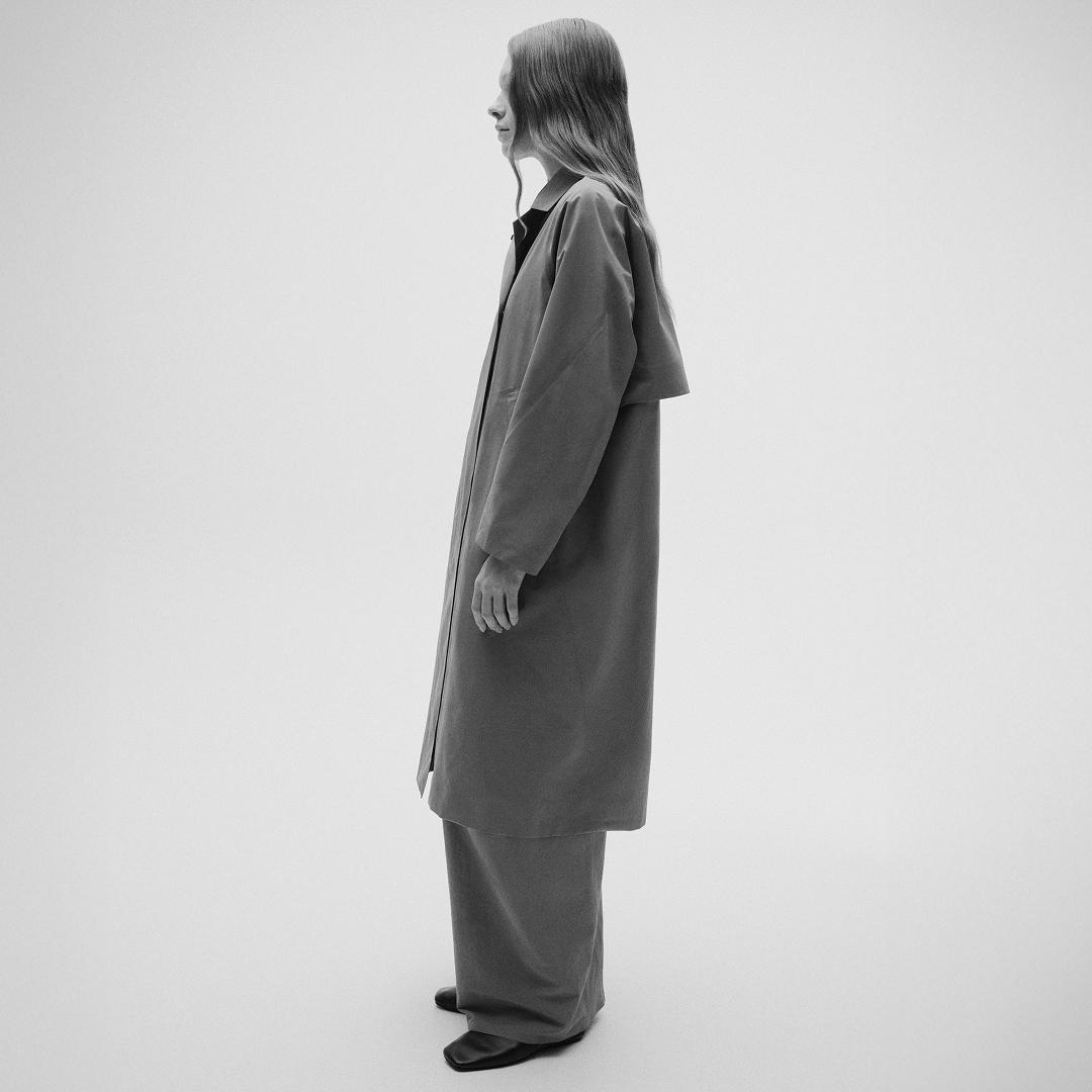 Black and white profile shot of a woman wearing a long coat and wide-leg pants.
