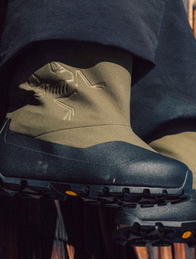 Olive green Arc'teryx boots with an embossed skeletal logo, dark rubber toe, and rugged Vibram sole, worn under dark pants.