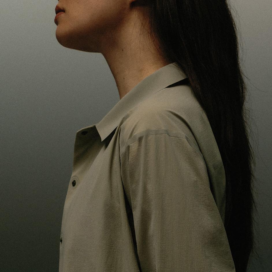 Profile of a person wearing a light green collared shirt with long dark hair.