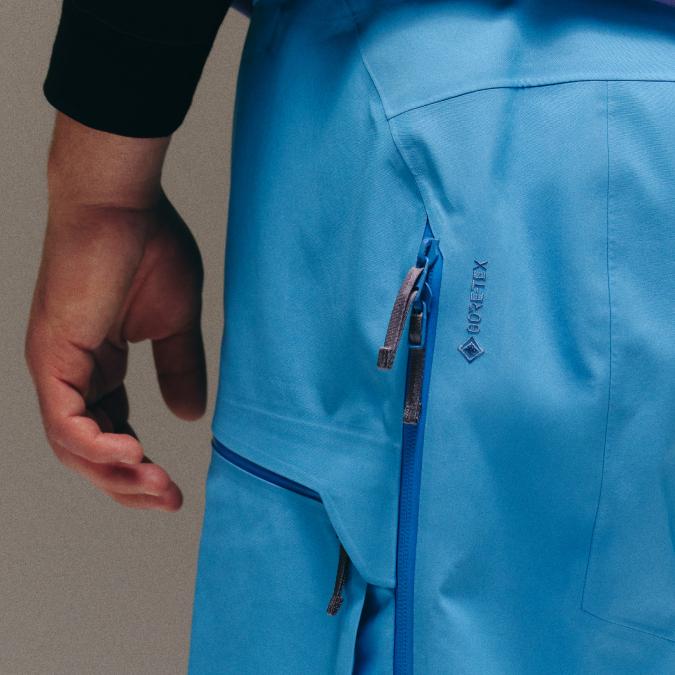 Close-up of a blue GORE-TEX garment with a zipper, next to a person's hand.