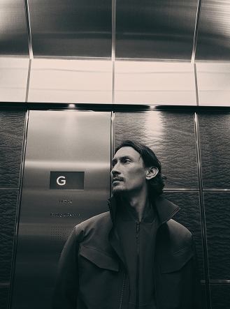 Monochrome shot of a man with a mustache in an elevator, looking to the side.