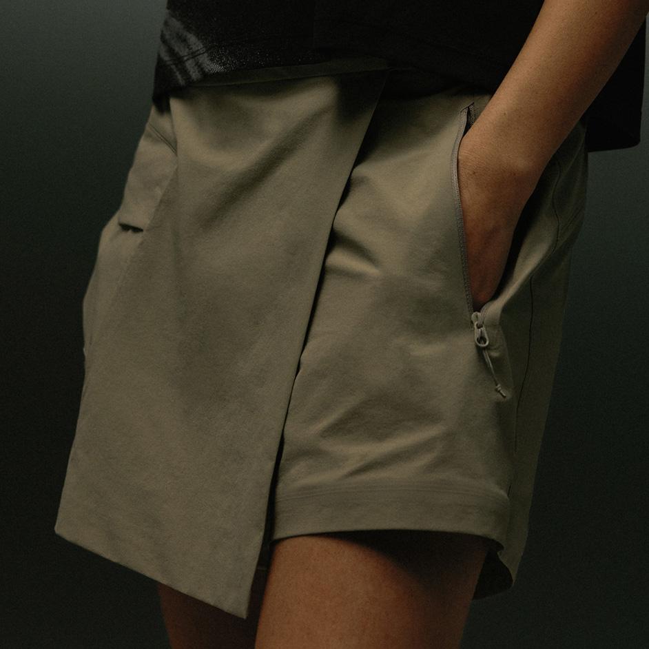 Olive wrap-front shorts with a hand in a zippered pocket.