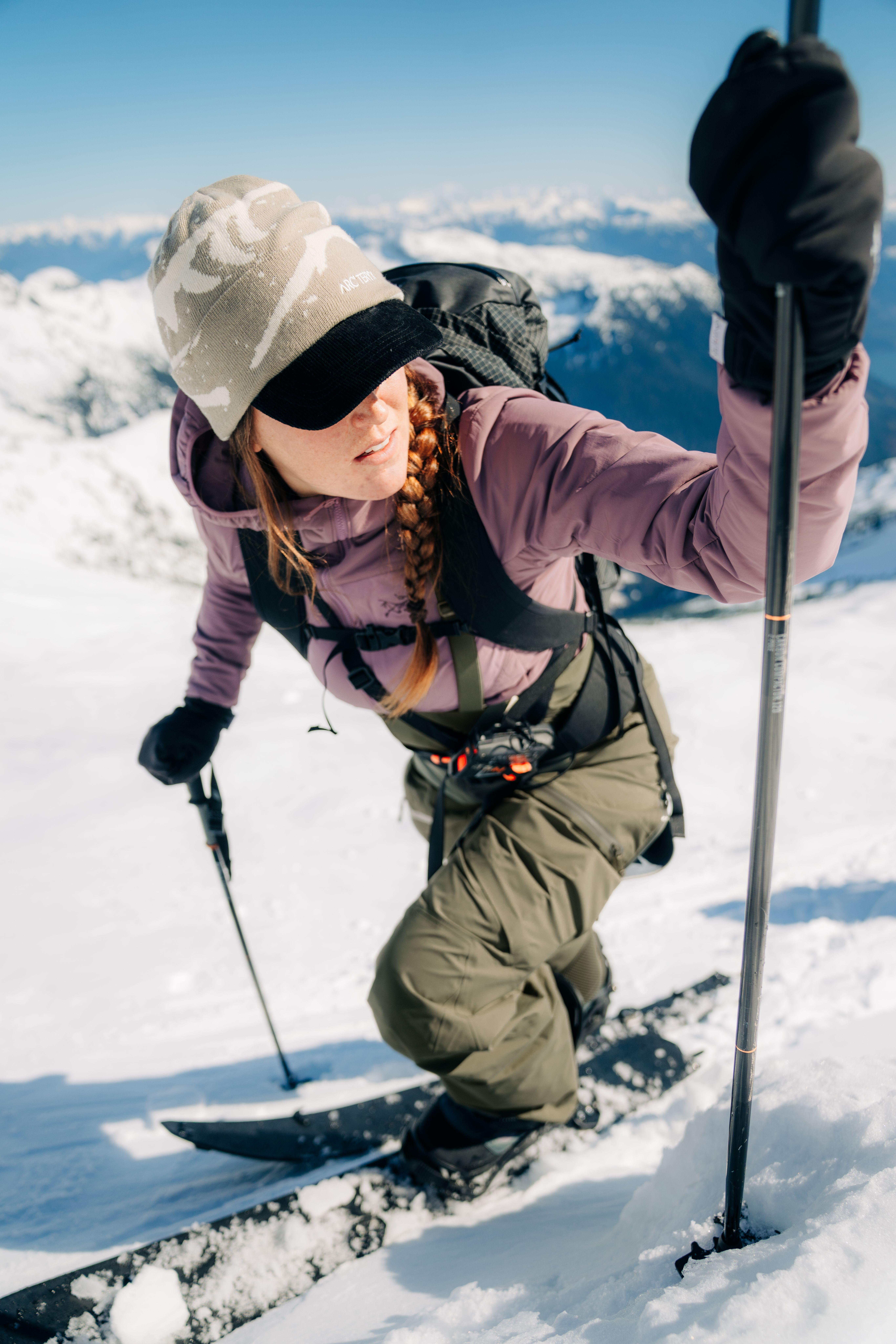 A woman with a red braid ski touring uphill on a snowy mountain.