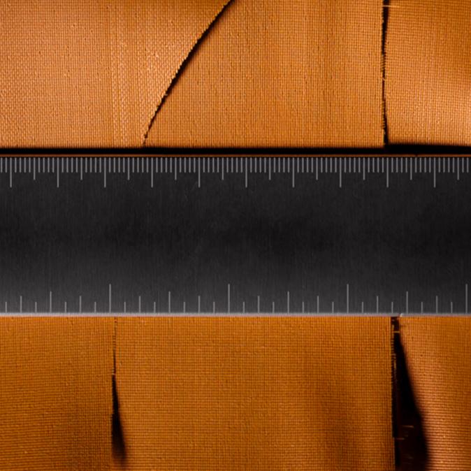 A dark gray ruler lies horizontally over textured orange fabric that is torn in several places.