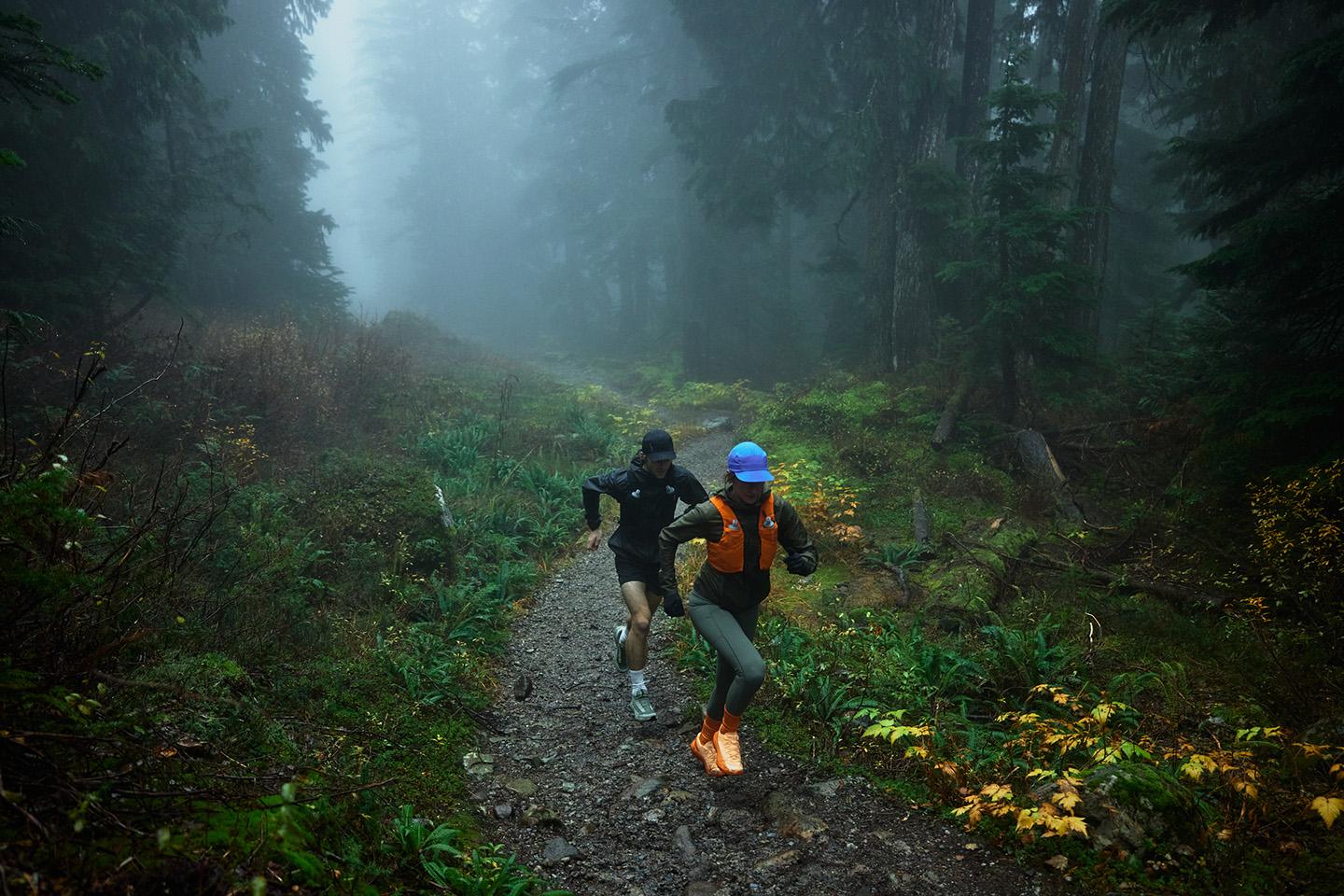 two people are running down a trail in the woods on a foggy day