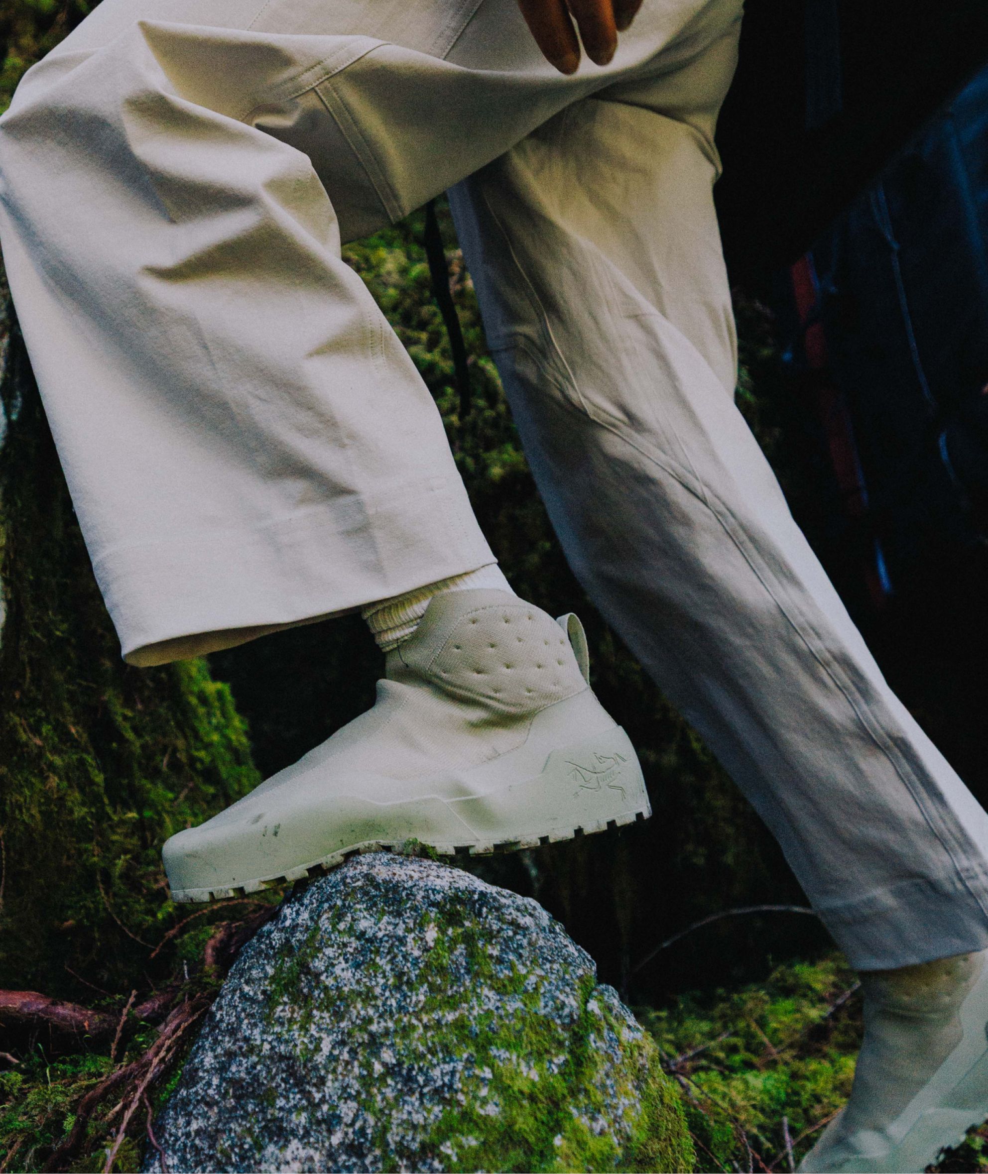 A person in beige pants and light green Arc'teryx boots steps on a mossy rock.
