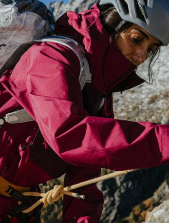 Close-up of a climber in a red jacket and helmet, with a yellow rope tied to their harness.