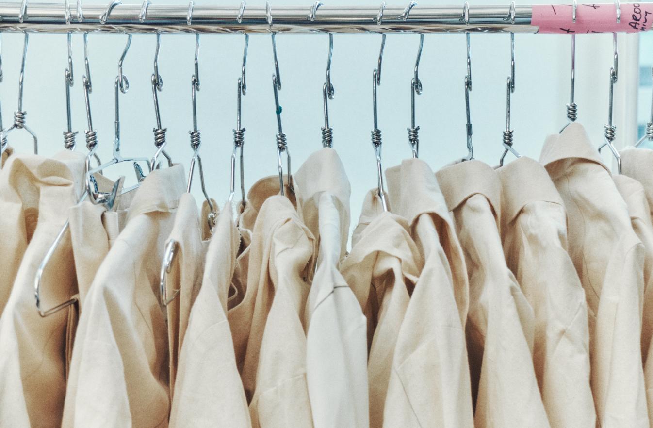 A row of light beige lab coats or uniform shirts hanging on a metal rack.