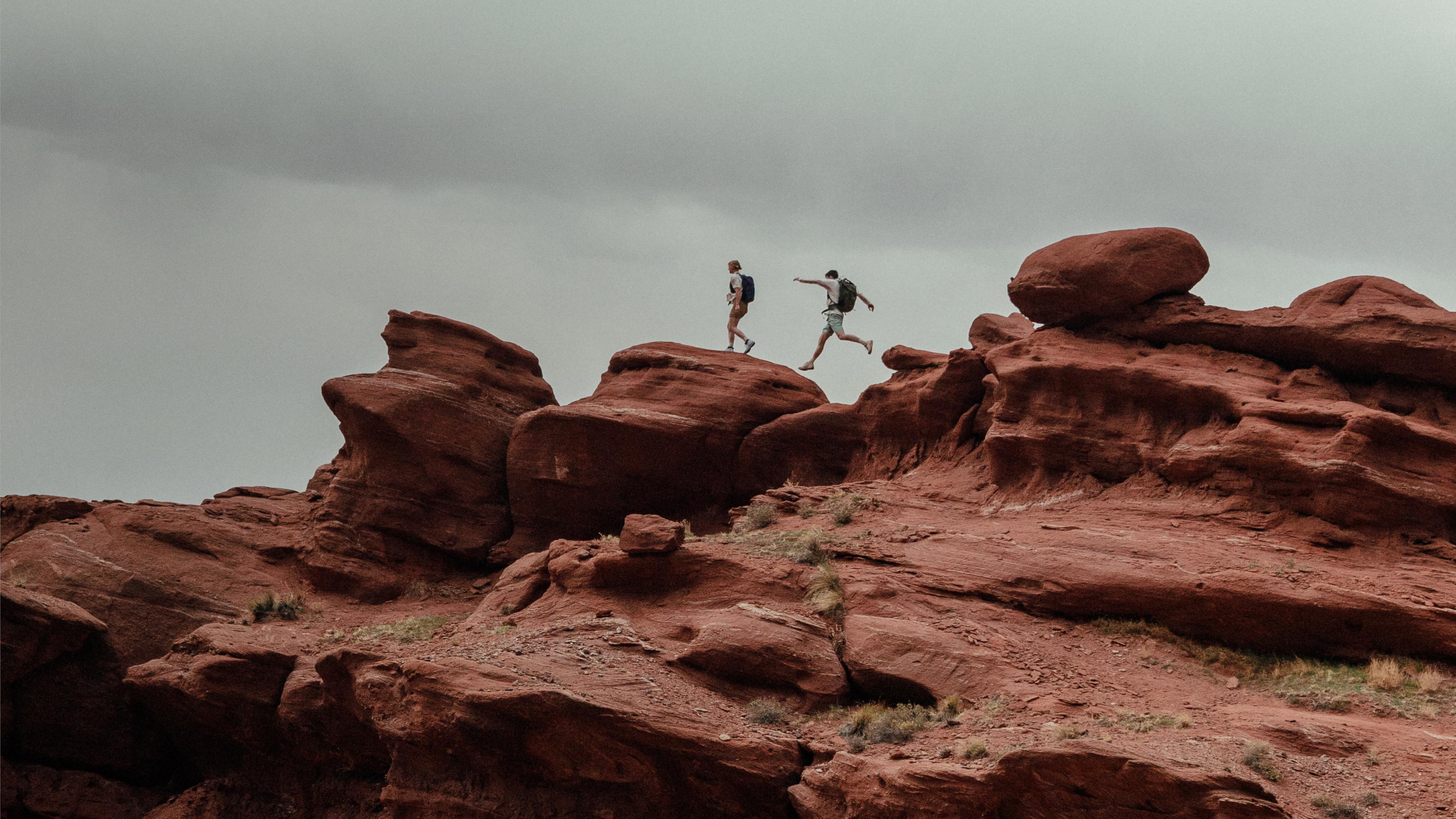 two people are walking on top of a rocky hill.