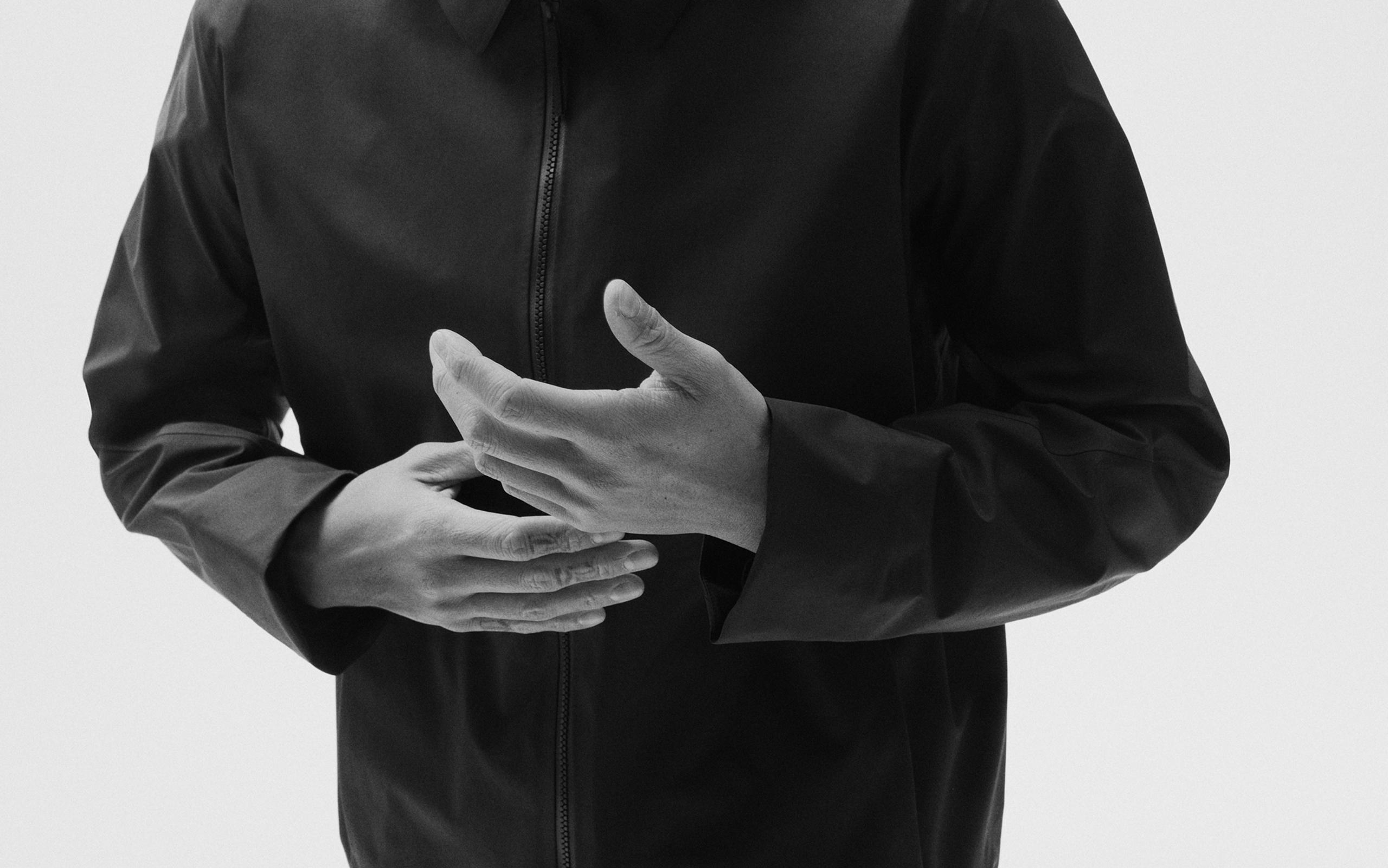 Monochrome shot of a person in a dark jacket with hands clasped.