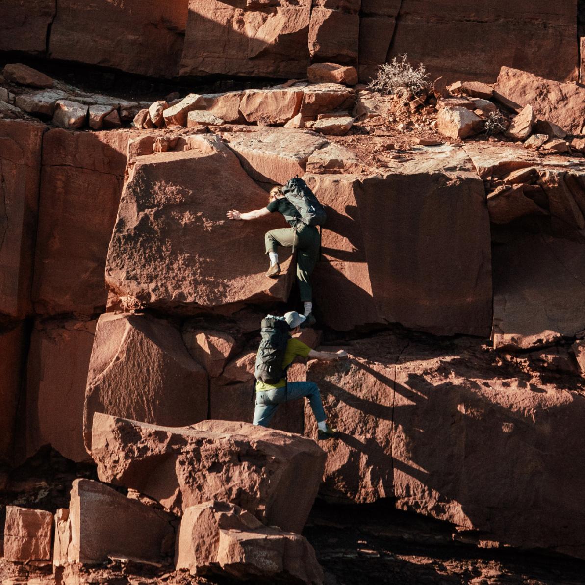 two people with backpacks are climbing up a rock wall .