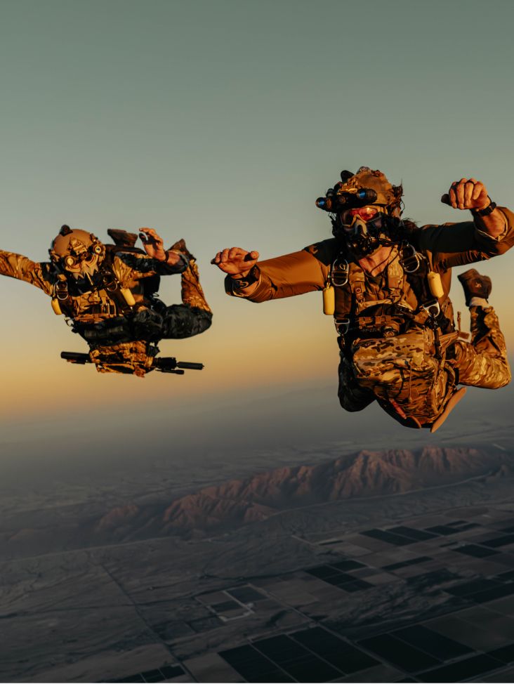 Two operators in tactical gear freefalling against a sunset sky over a desert.