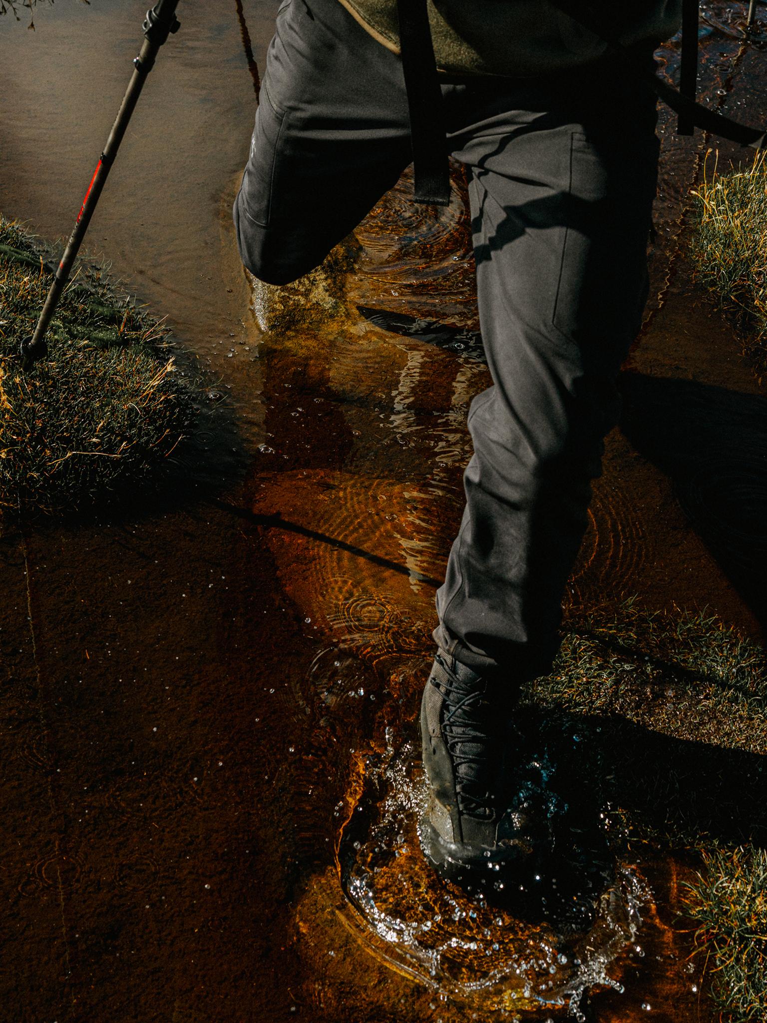 A hiker's boot splashes through shallow, reddish-brown water.