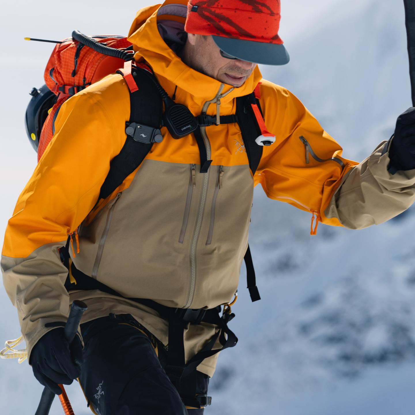 a man wearing a backpack and an orange jacket is walking through the snow .