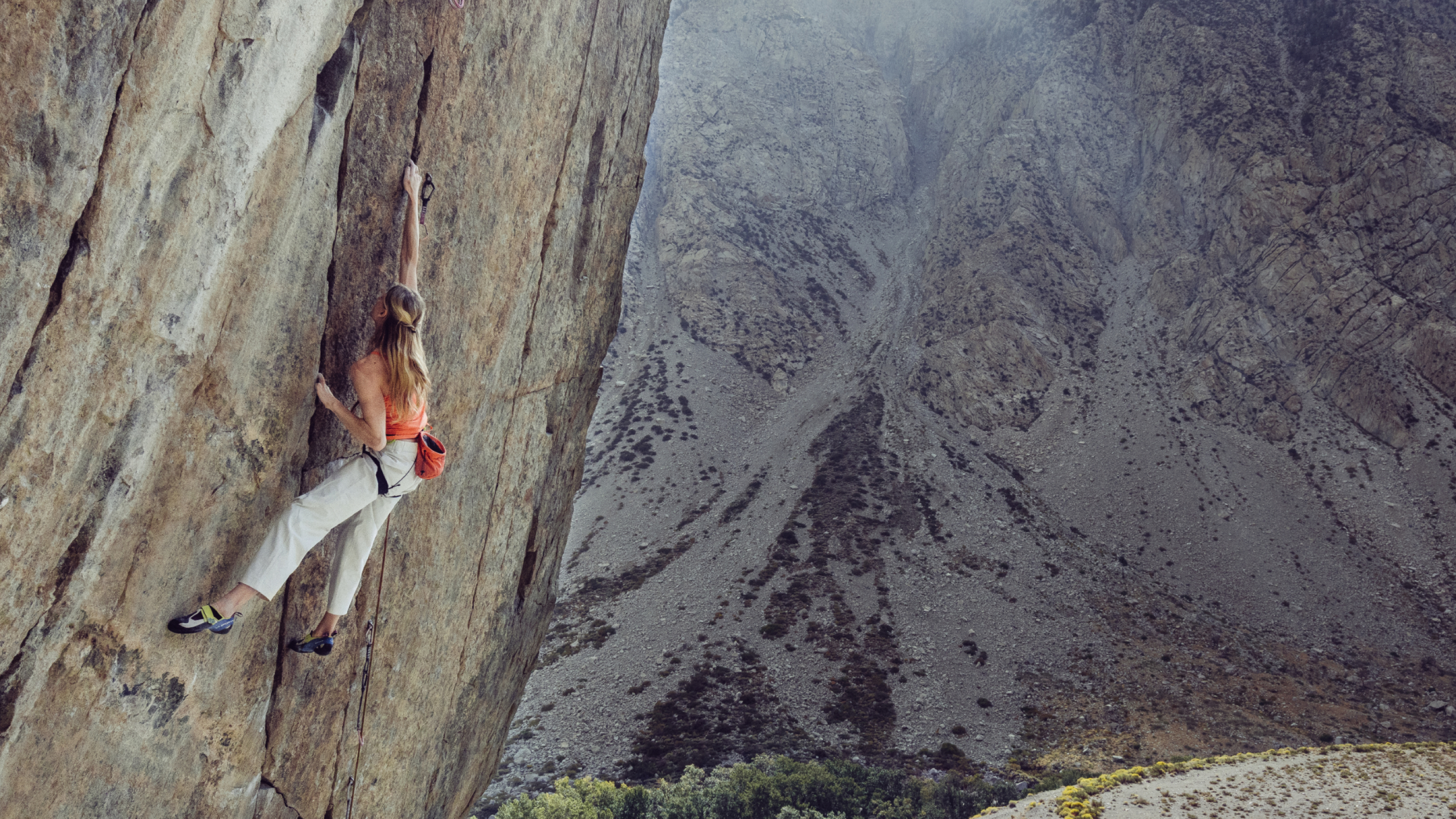 A woman rock climbing a steep rock face with a rocky mountain in the background.