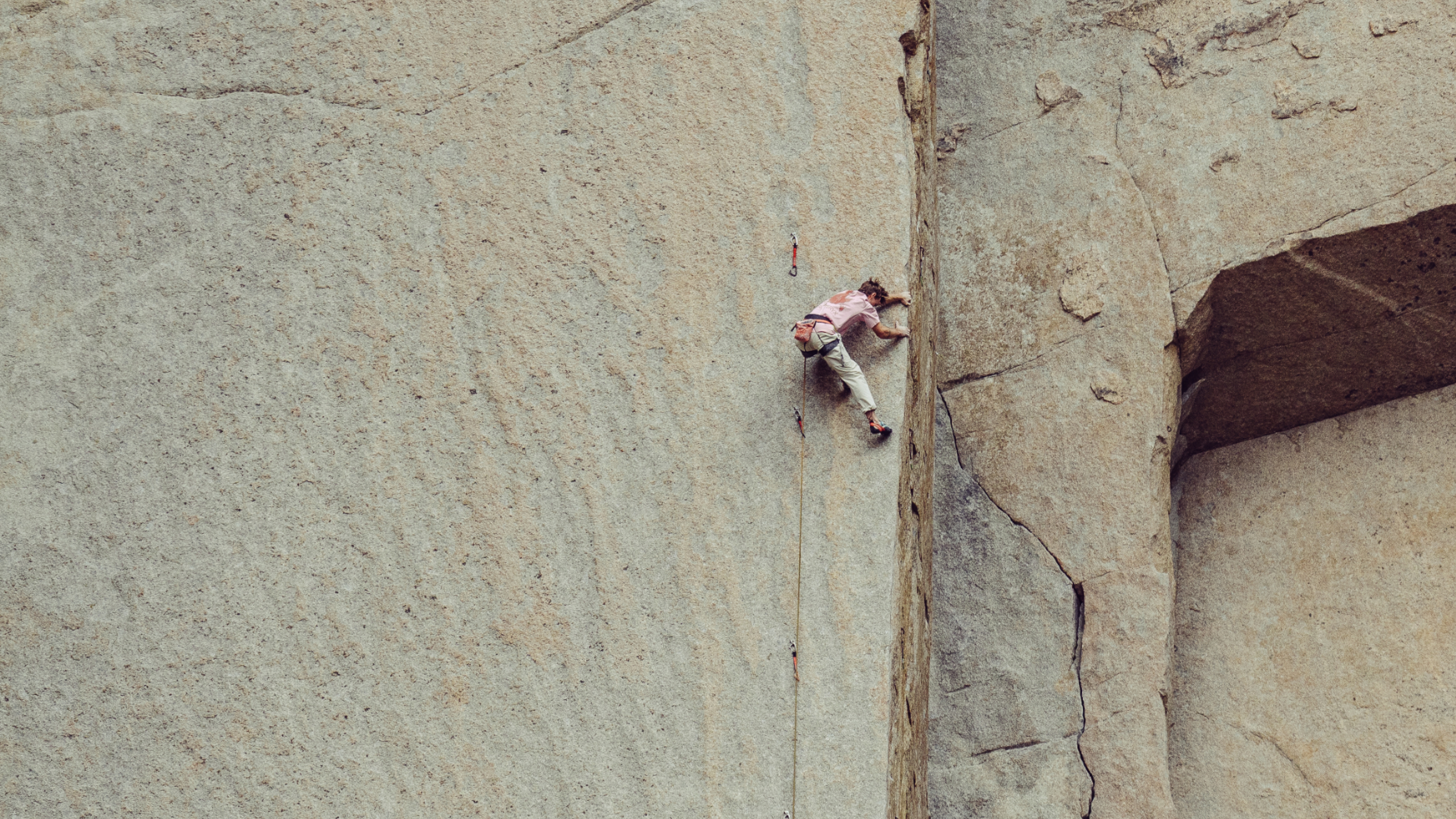 A rock climber ascending a massive, light-colored rock wall.