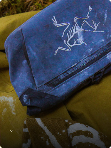 Close-up of a worn blue Arc'teryx bag with a white skeleton logo, resting on olive green fabric.