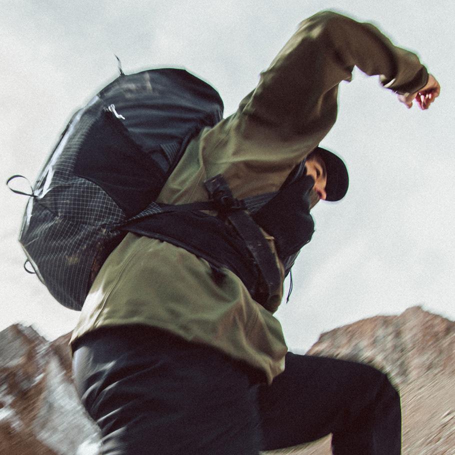 Hiker with a backpack and hat ascending rocky terrain.