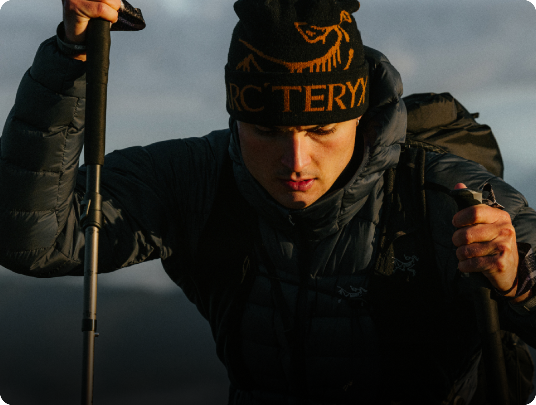A hiker wearing an Arc'teryx beanie and jacket, holding trekking poles.