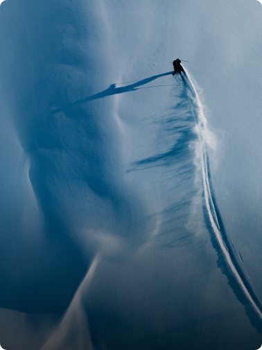 Aerial view of a skier carving a turn in deep blue snow, kicking up a large plume of powder.