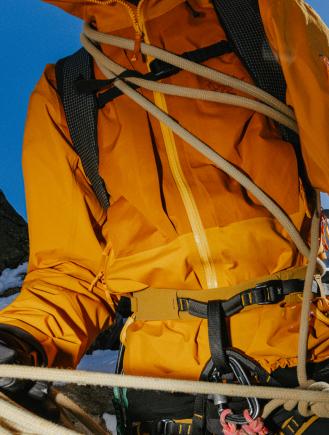 Climber in orange jacket with harness and ropes in snowy mountains.
