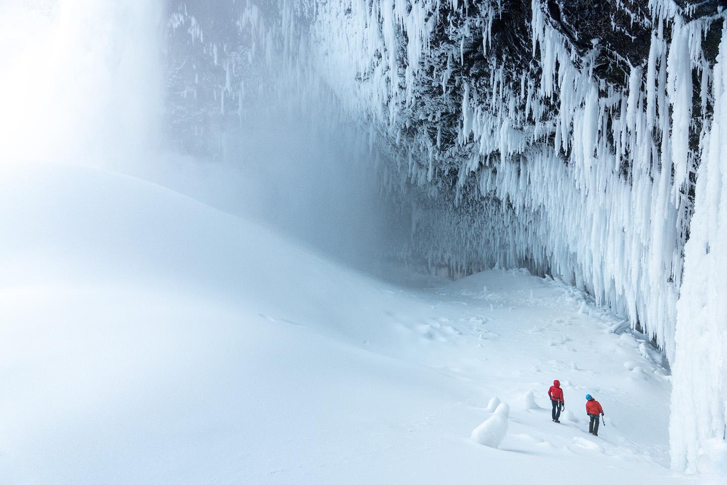 two people are walking in the snow near a waterfall covered in ice