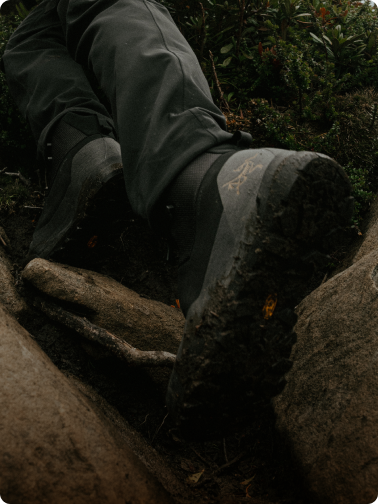 Muddy Arc'teryx hiking boots stepping on a rocky trail.