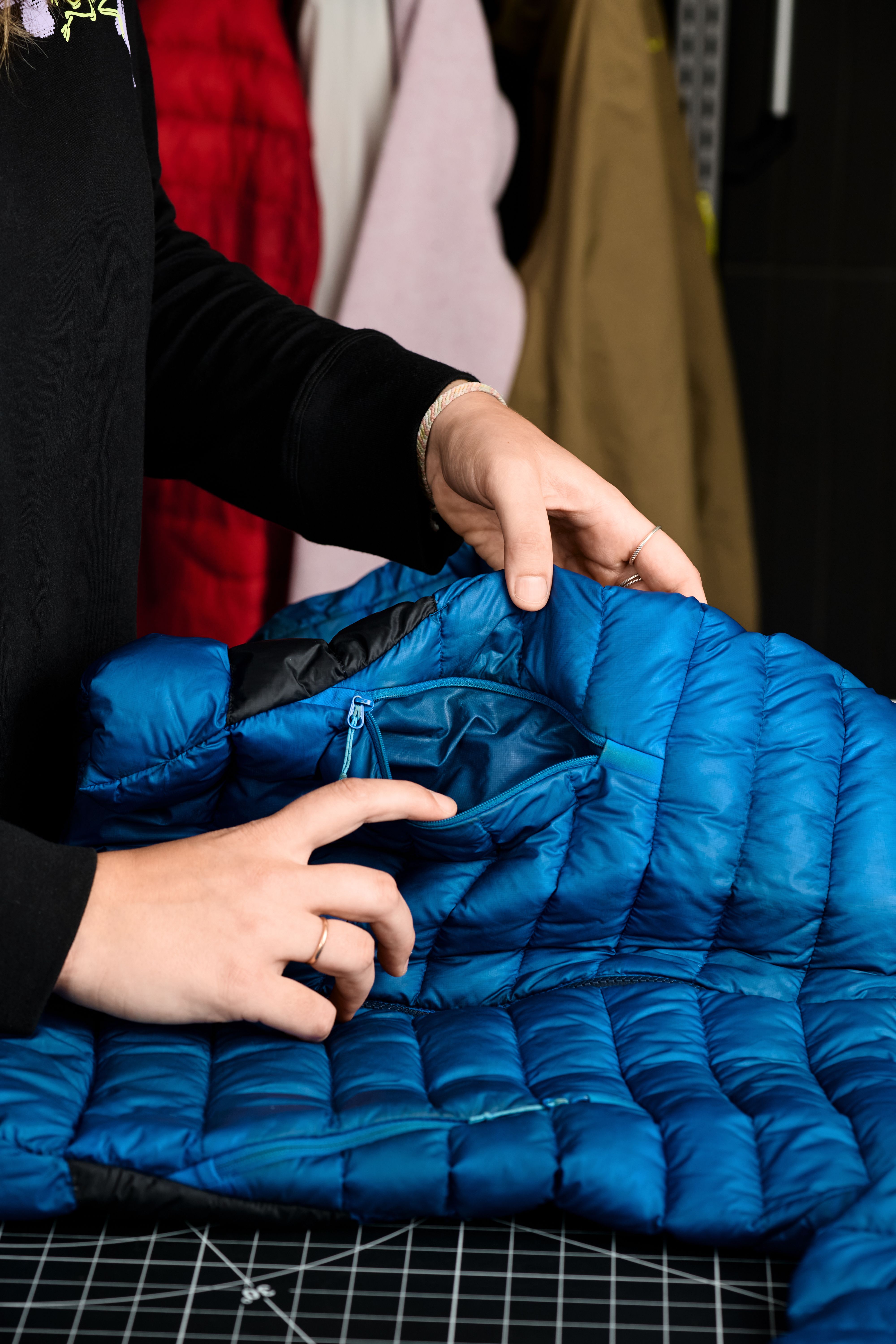 A person's hands open a zippered pocket on a blue puffer jacket.