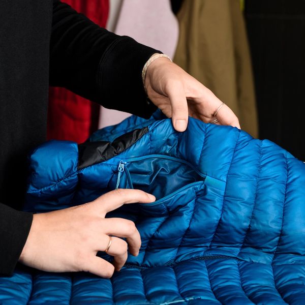 A person's hands open a zippered pocket on a blue puffer jacket.