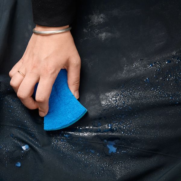 A hand holding a blue sponge wipes water from a dark, possibly waterproof, surface.
