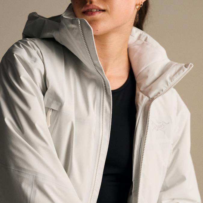 A person wears a light grey Arc'teryx hooded jacket over a black top.