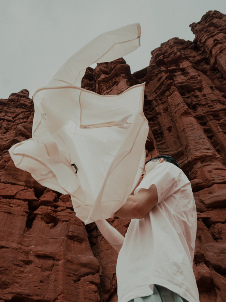A person holds a white, billowing fabric against a backdrop of red rock cliffs.
