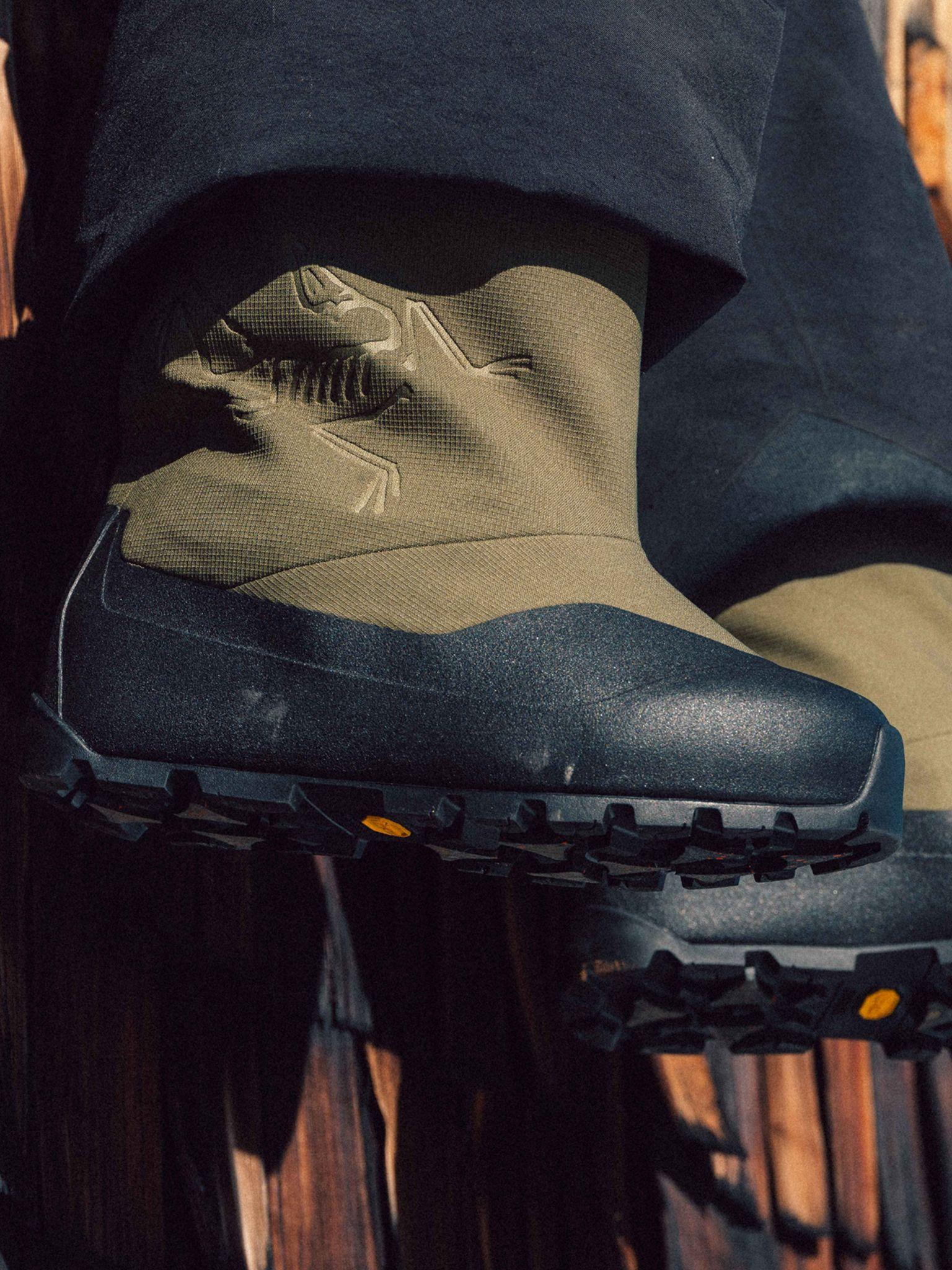 Arc'teryx olive green boots with black rubberized toes, an embossed logo, and black Vibram soles, worn with dark pants.