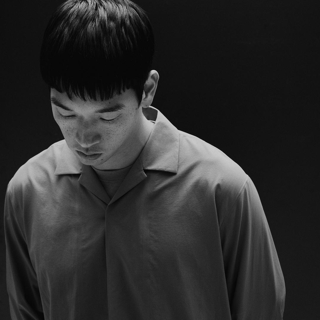 Monochrome portrait of a young person with freckles looking down, wearing a collared shirt.