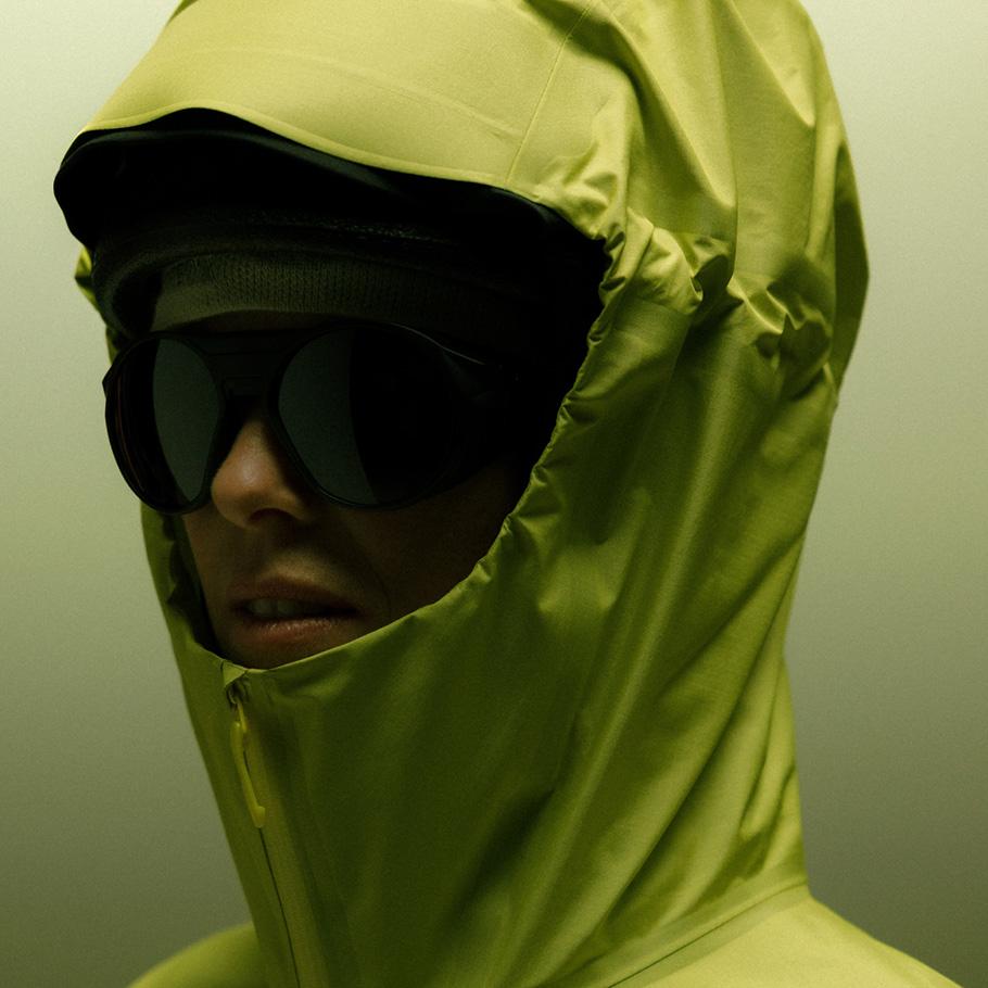 Person wearing a lime green hooded jacket and dark sunglasses.