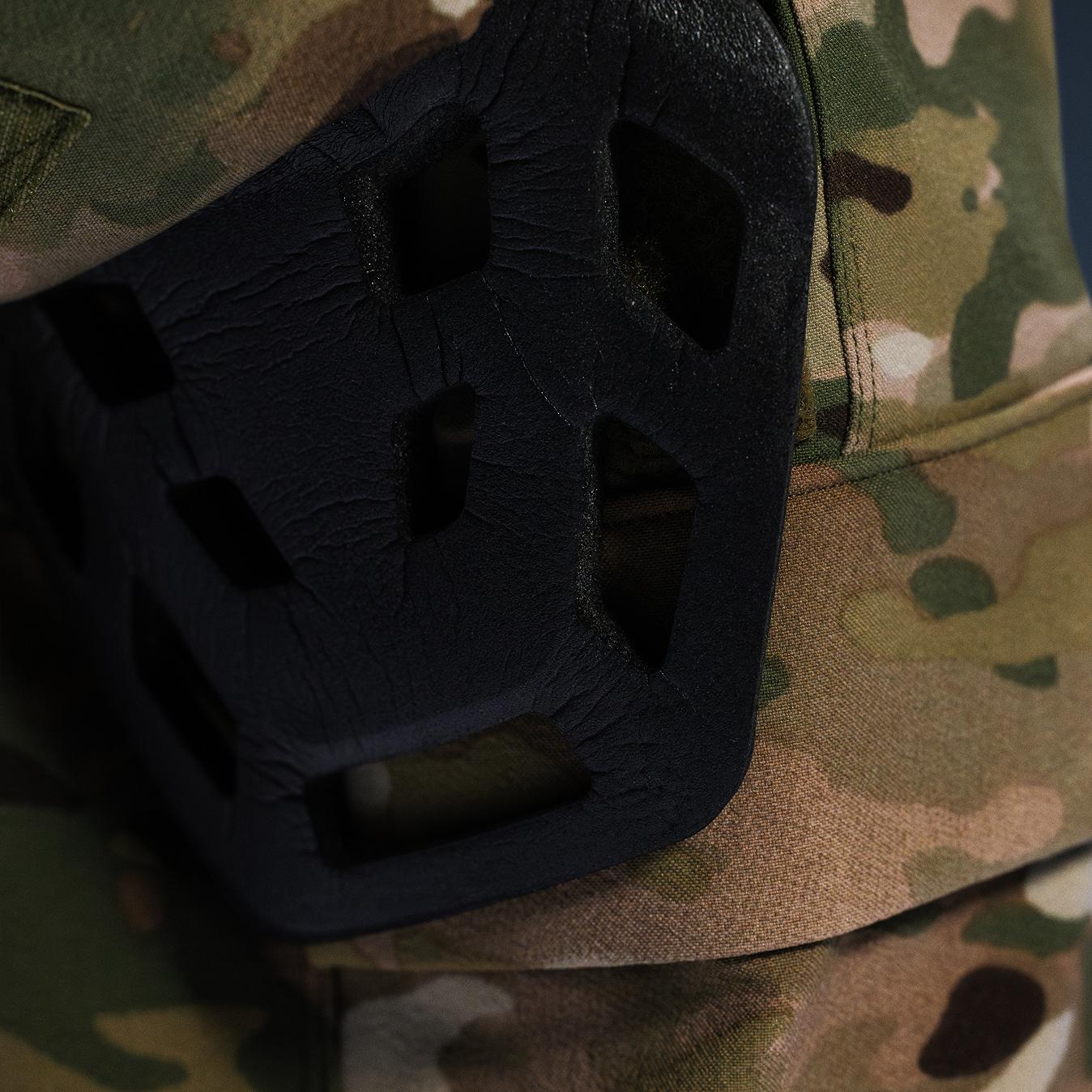 Black textured knee pad with geometric cutouts on camouflage fabric.
