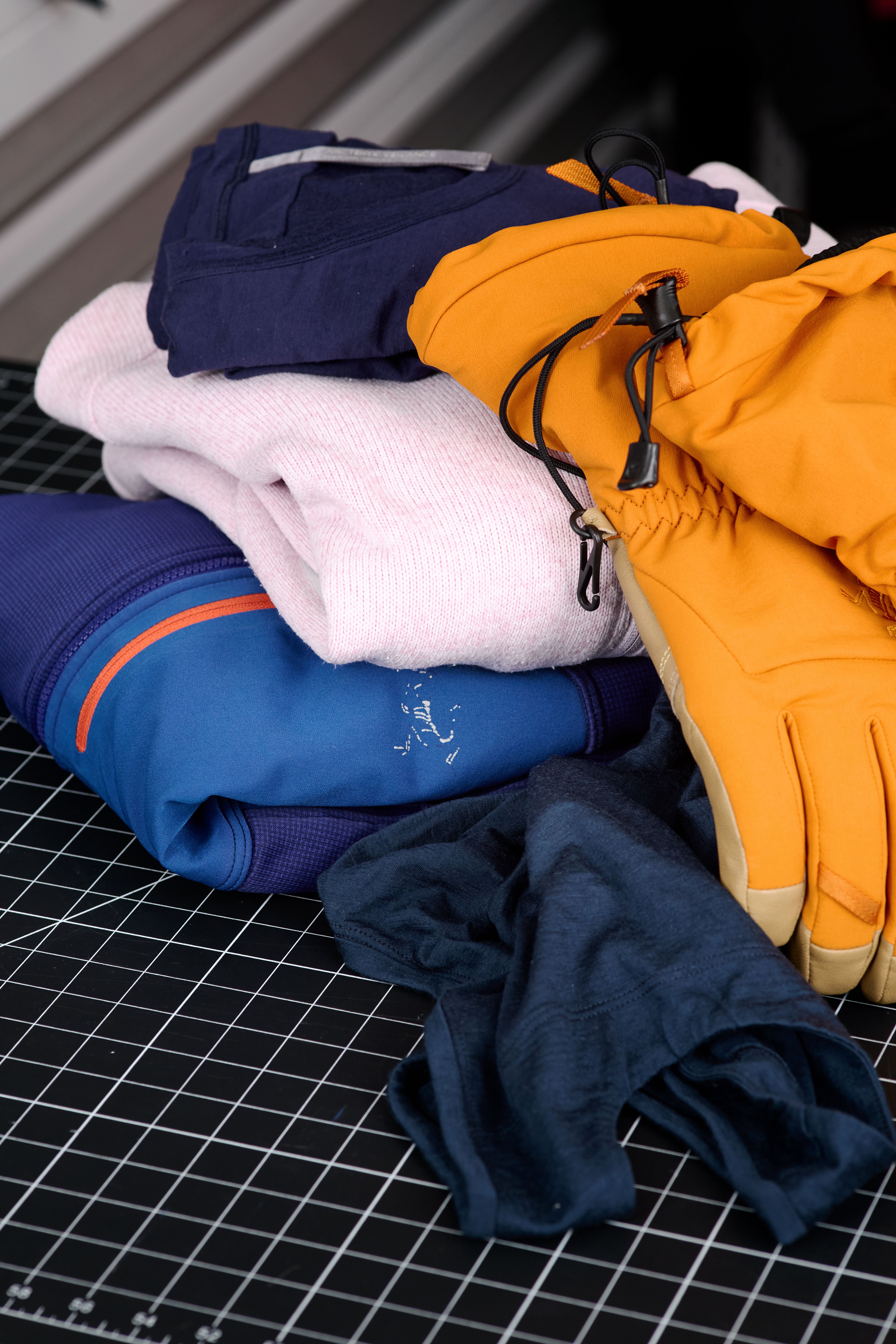 Outdoor clothing and ski gloves stacked on a black grid mat.