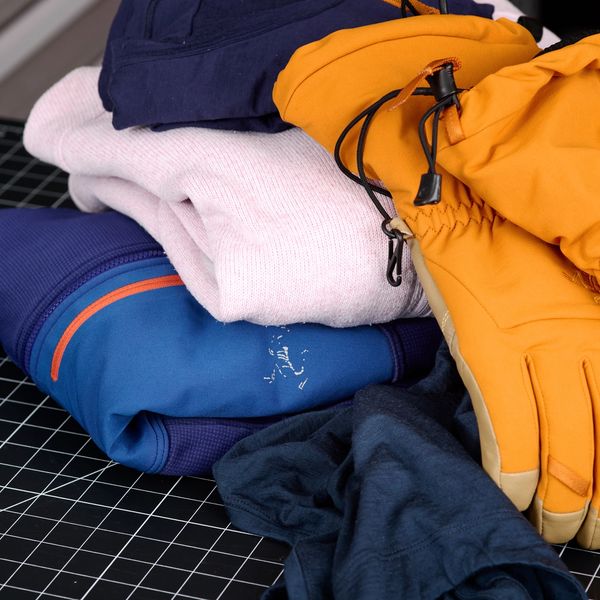 Outdoor clothing and ski gloves stacked on a black grid mat.