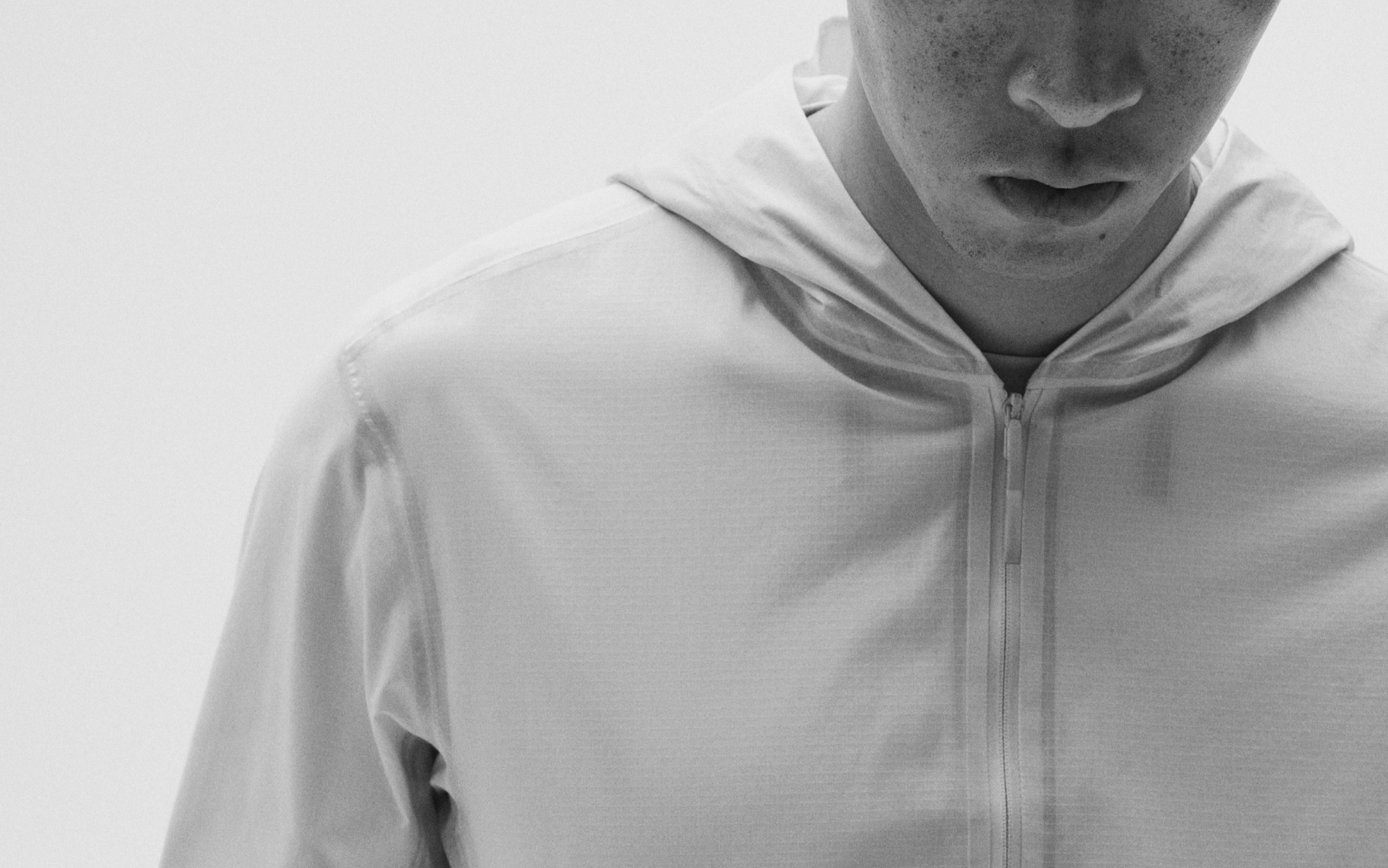 Close-up, monochrome shot of a person in a light hooded jacket, looking down.