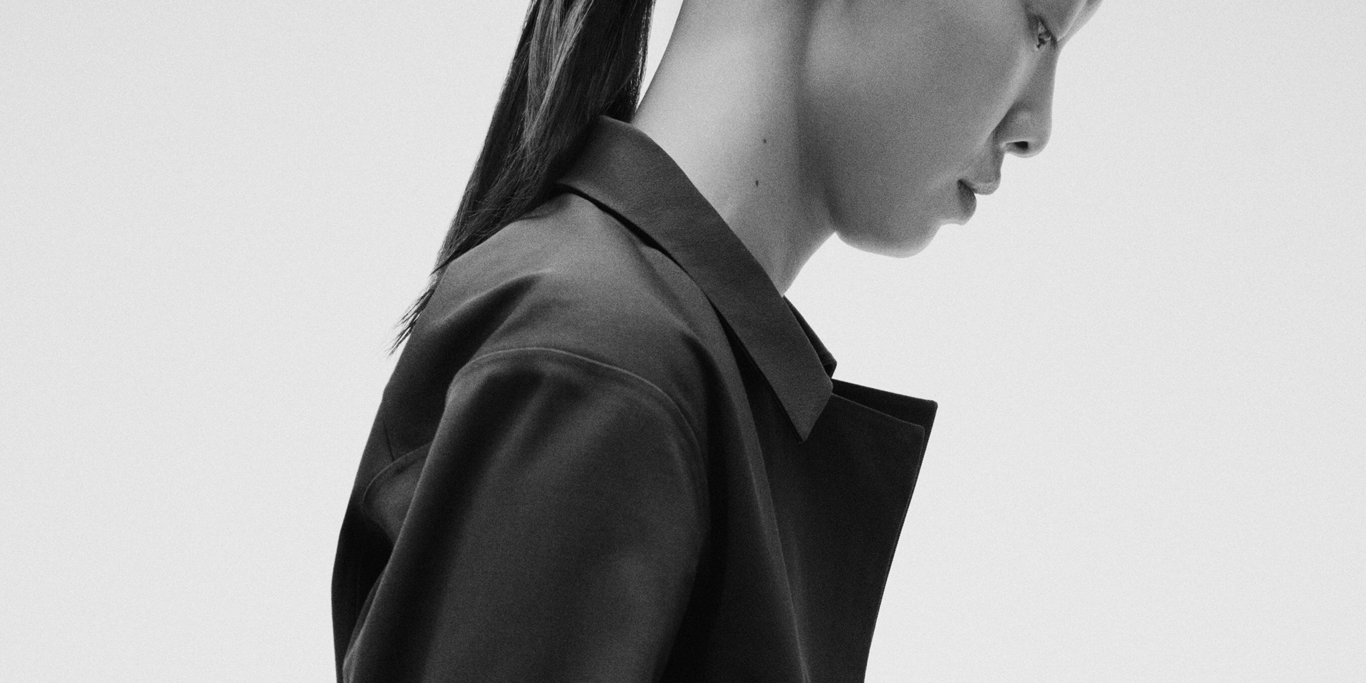 a black and white photo of a woman wearing a black jacket and a ponytail .