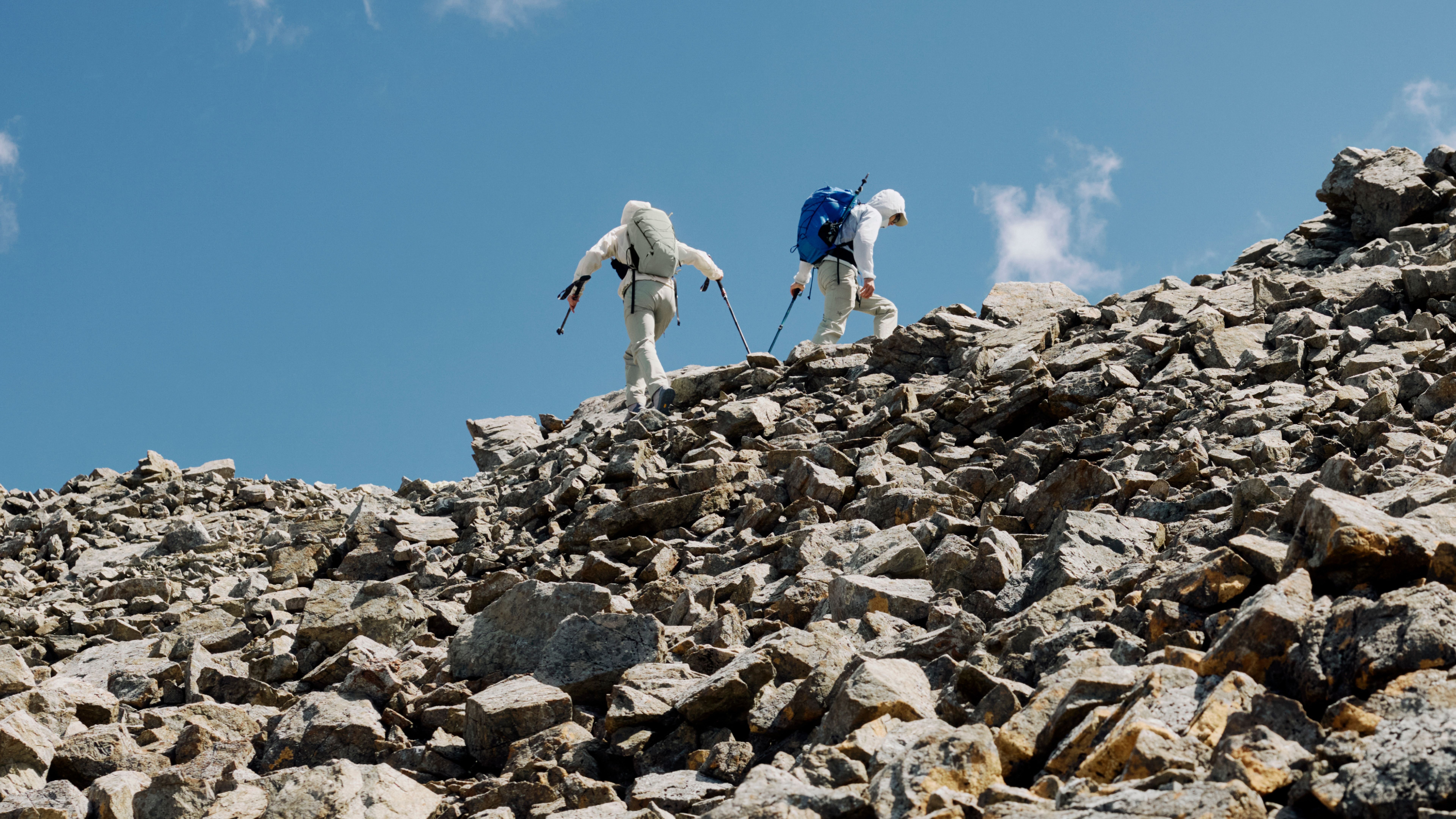 Two hikers ascend a steep, rocky mountain under a clear blue sky.