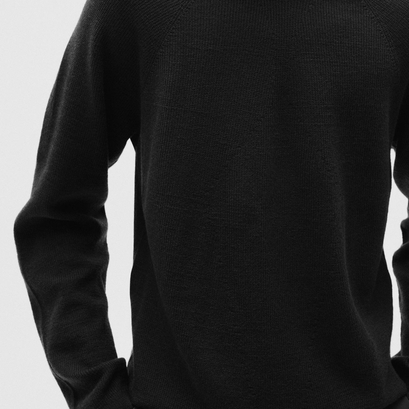 a close up of a person wearing a black sweater with their hands in their pockets.