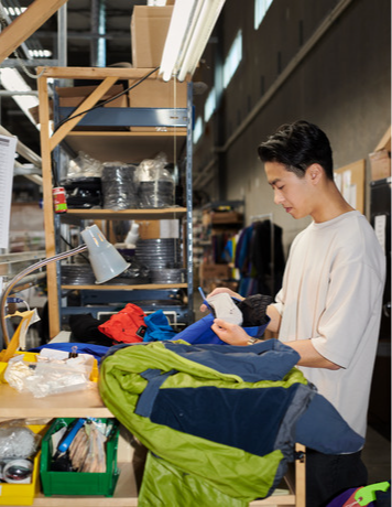 A young man inspects outdoor gear on a workbench in a workshop.