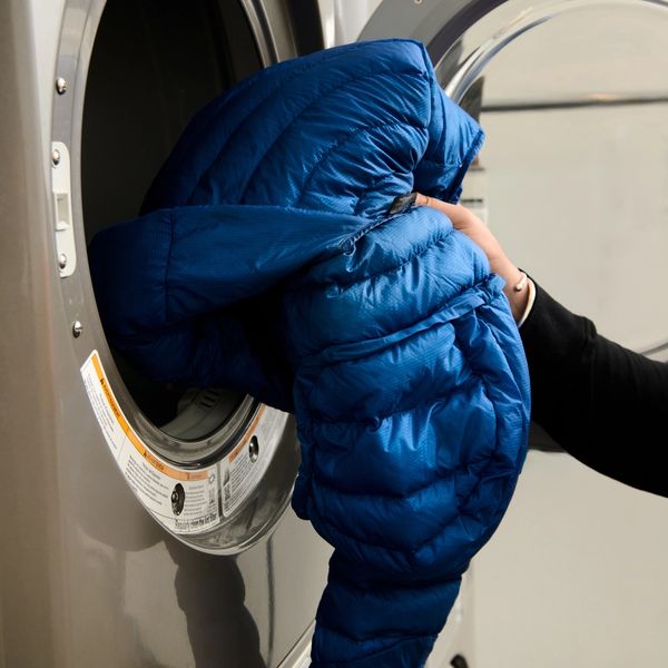 A hand pulls a blue puffer jacket from a front-loading dryer.