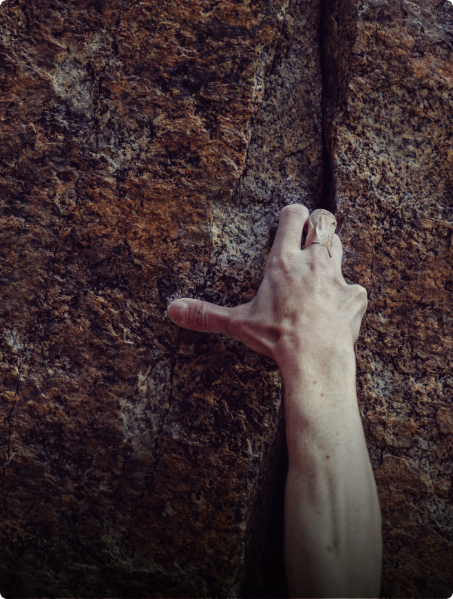 A climber's hand gripping a narrow crack in a textured rock face.